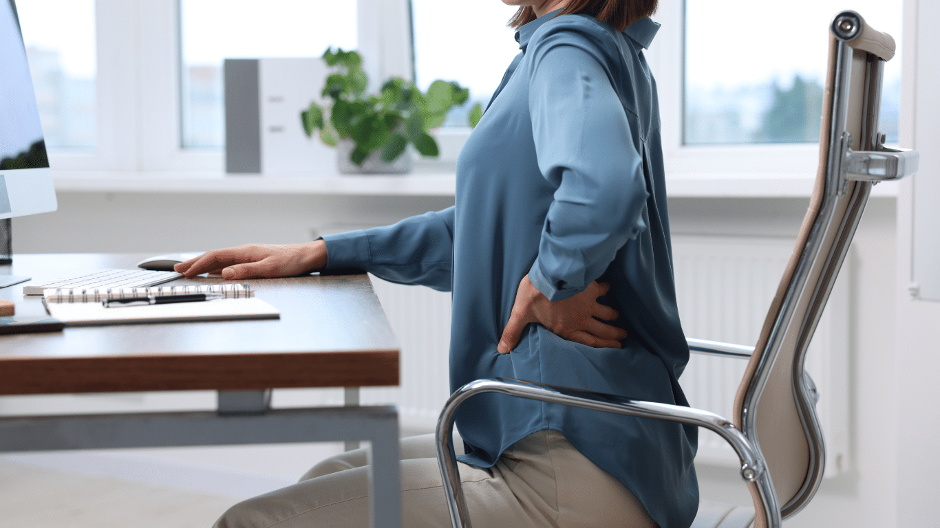 Woman at a desk holding her lower back